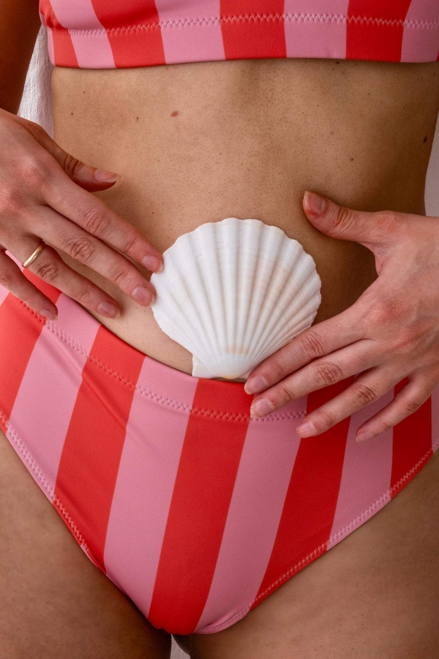 Peach Pink Stripe High Waisted Bikini Set details in close up and shell held in front of belly buttom